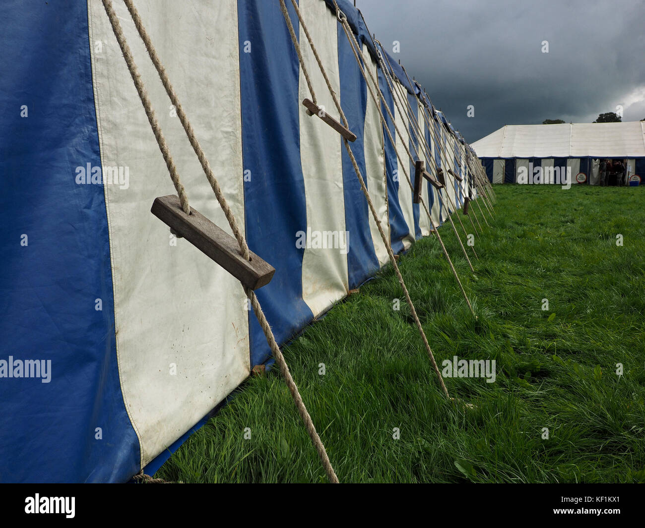 blue and white striped marquee with guy ropes in field with dark grey sky looming behind at rural show in Cumbria,England UK Stock Photo