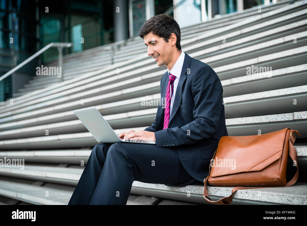 Young businessman using a laptop while sitting down outdoors Stock ...