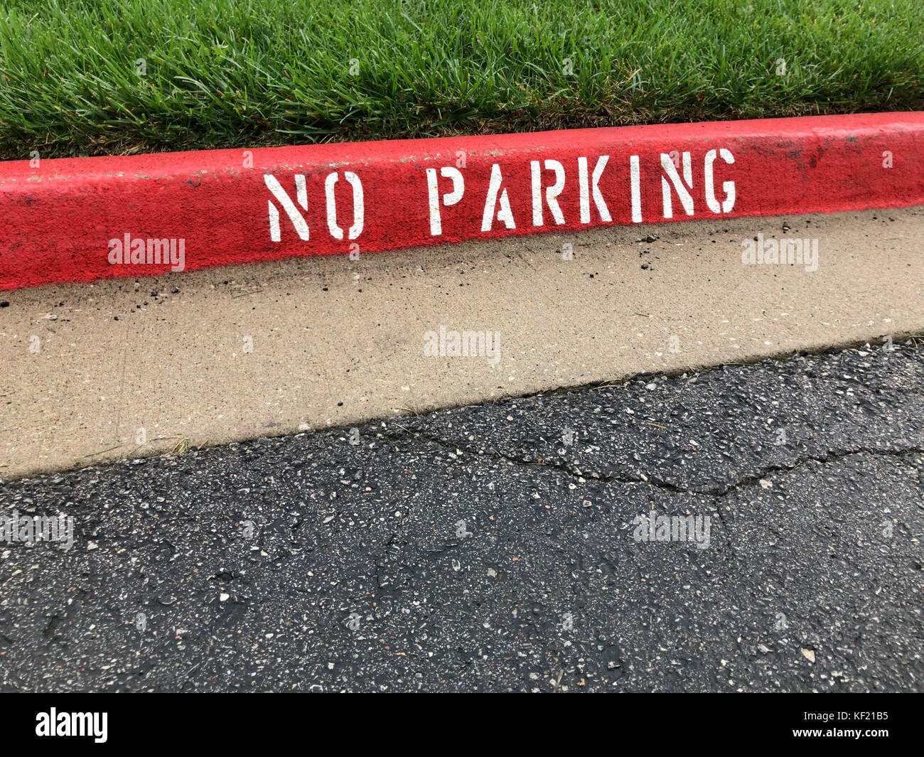 Red stenciled no parking zone curb sign with green grass and asphalt Stock Photo