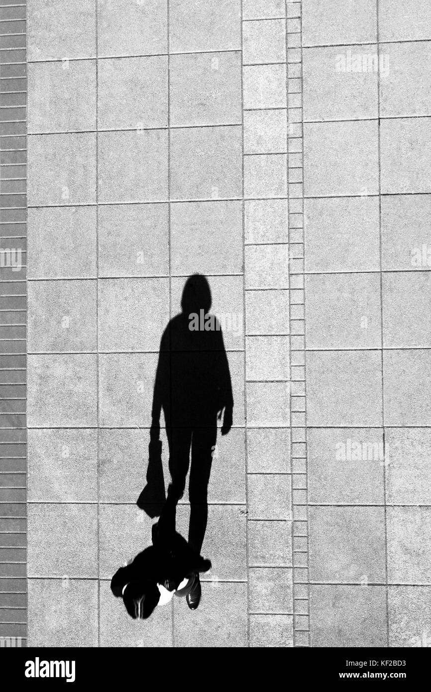 Shadow of a woman walking and holding a bag , on city sidewalk from above in black and white Stock Photo