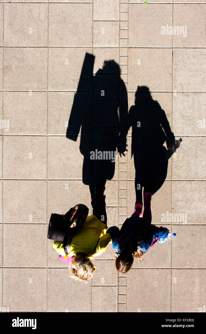 Shadow of a mother and daughter walking hand in hand , on city sidewalk from above Stock Photo