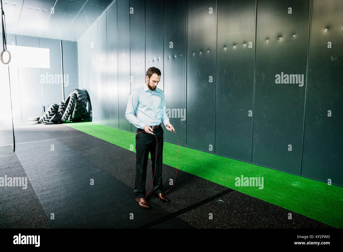 Businessman in gym looking at skipping rope Stock Photo