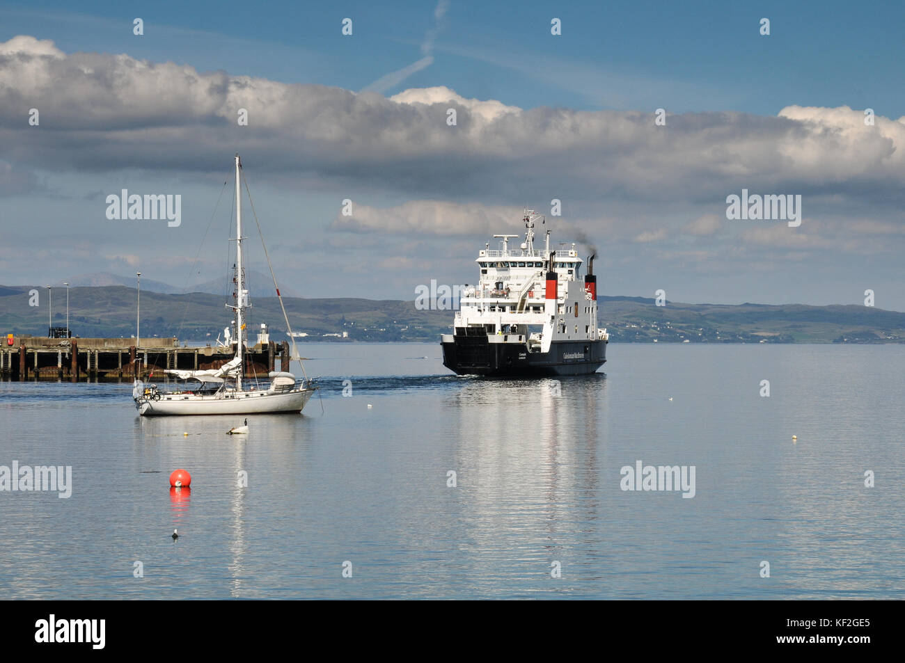 View across the still waters of Mallaig harbour on the Scottish west coast in summer with moored boats, a ferry to the isles and blue sky Stock Photo