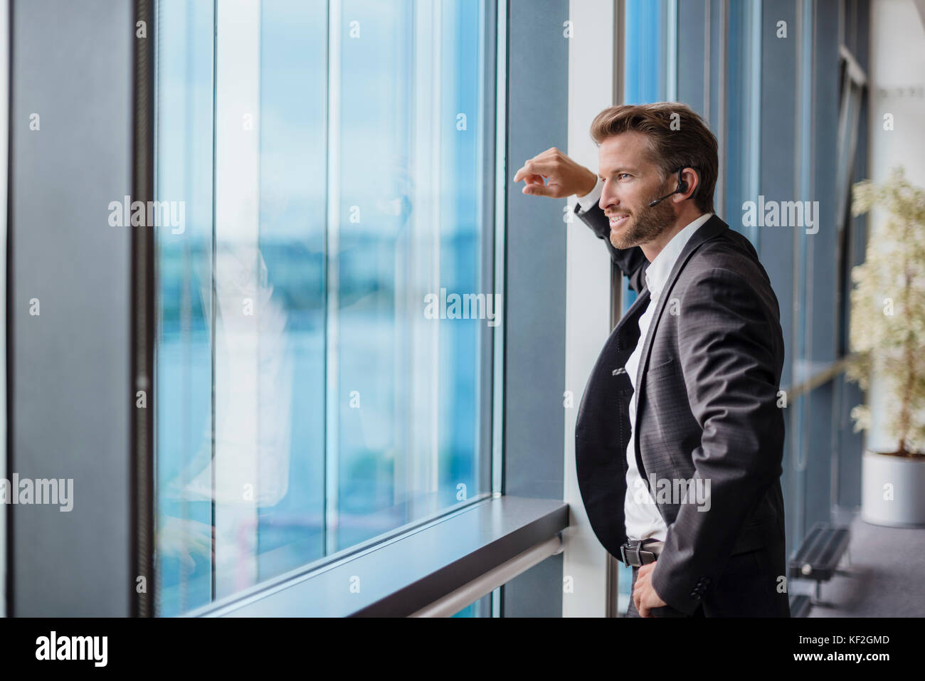 Relaxed businessman with bluetooth headset standing in his office looking out of the window Stock Photo