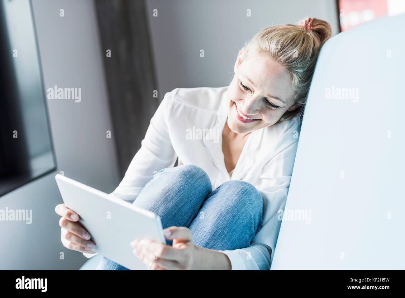 Smiling woman sitting on couch using tablet Stock Photo - Alamy