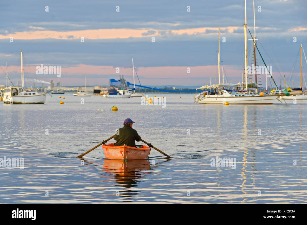 man rowing boat ashore in in quite waters of marina at dusk Stock Photo