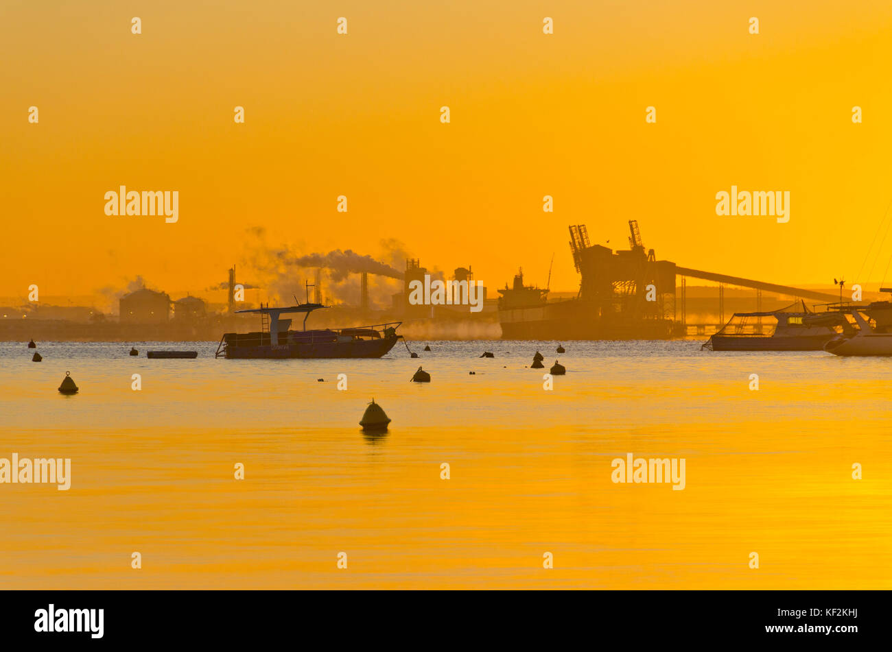 Boat at anchor in mussel farm with industry in background at sunrise Stock Photo