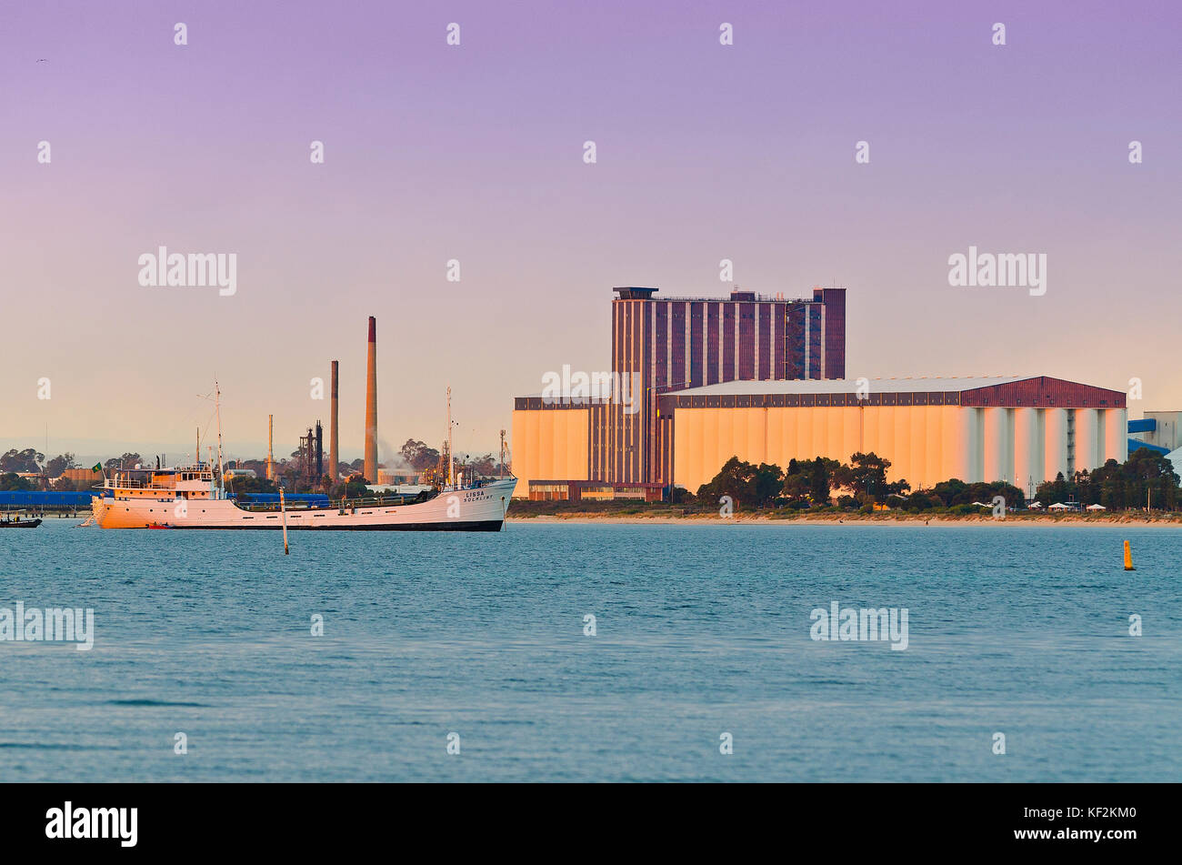 White ship at anchor in quiet harbour early in the morning with Kwinana Bulk Grain Handling Facility in background Stock Photo