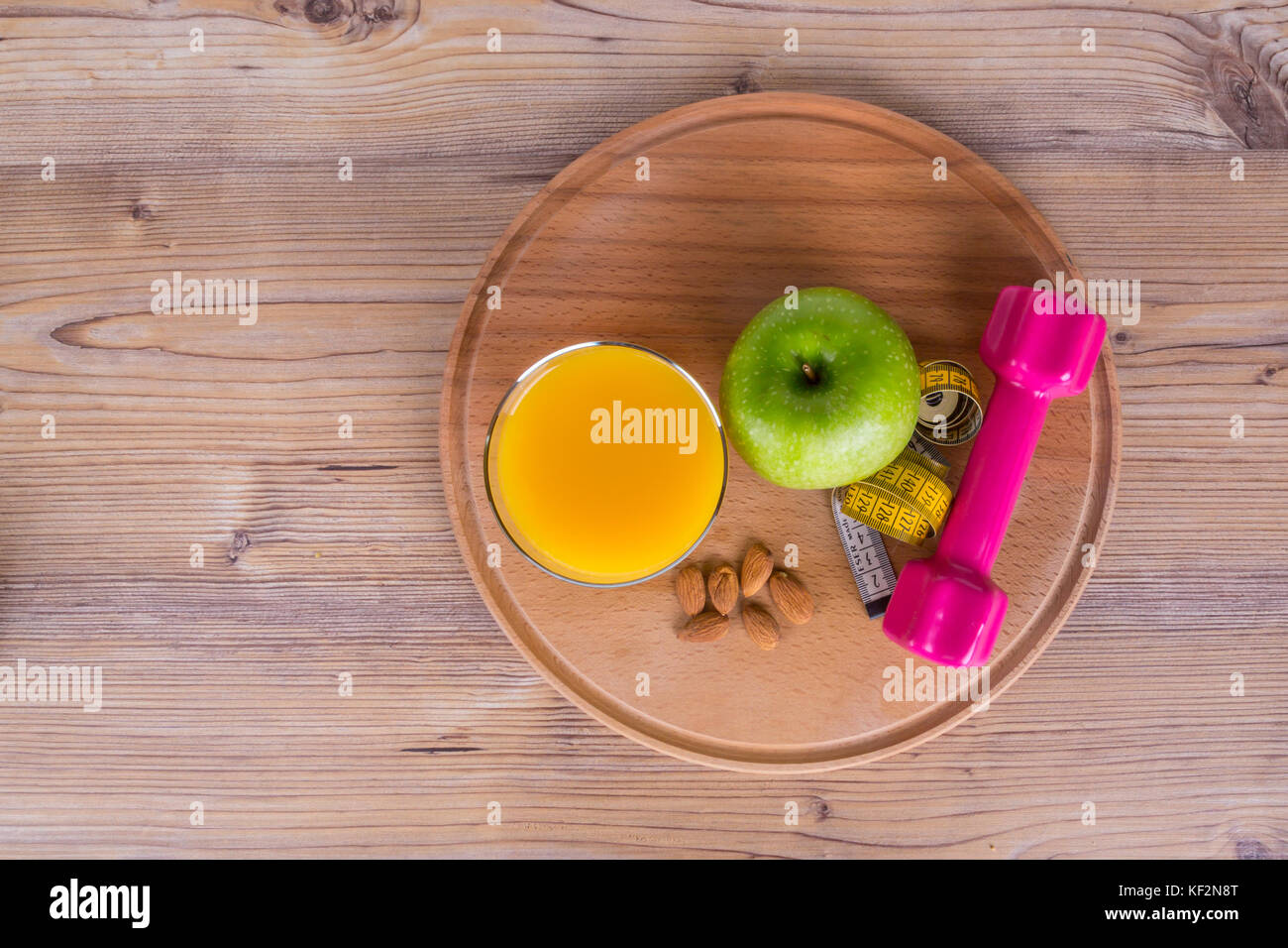 Close up top view of fruits, almond and orange juice, light weight and green apple, measurement tape with healthy fit concept on wooden background. Stock Photo