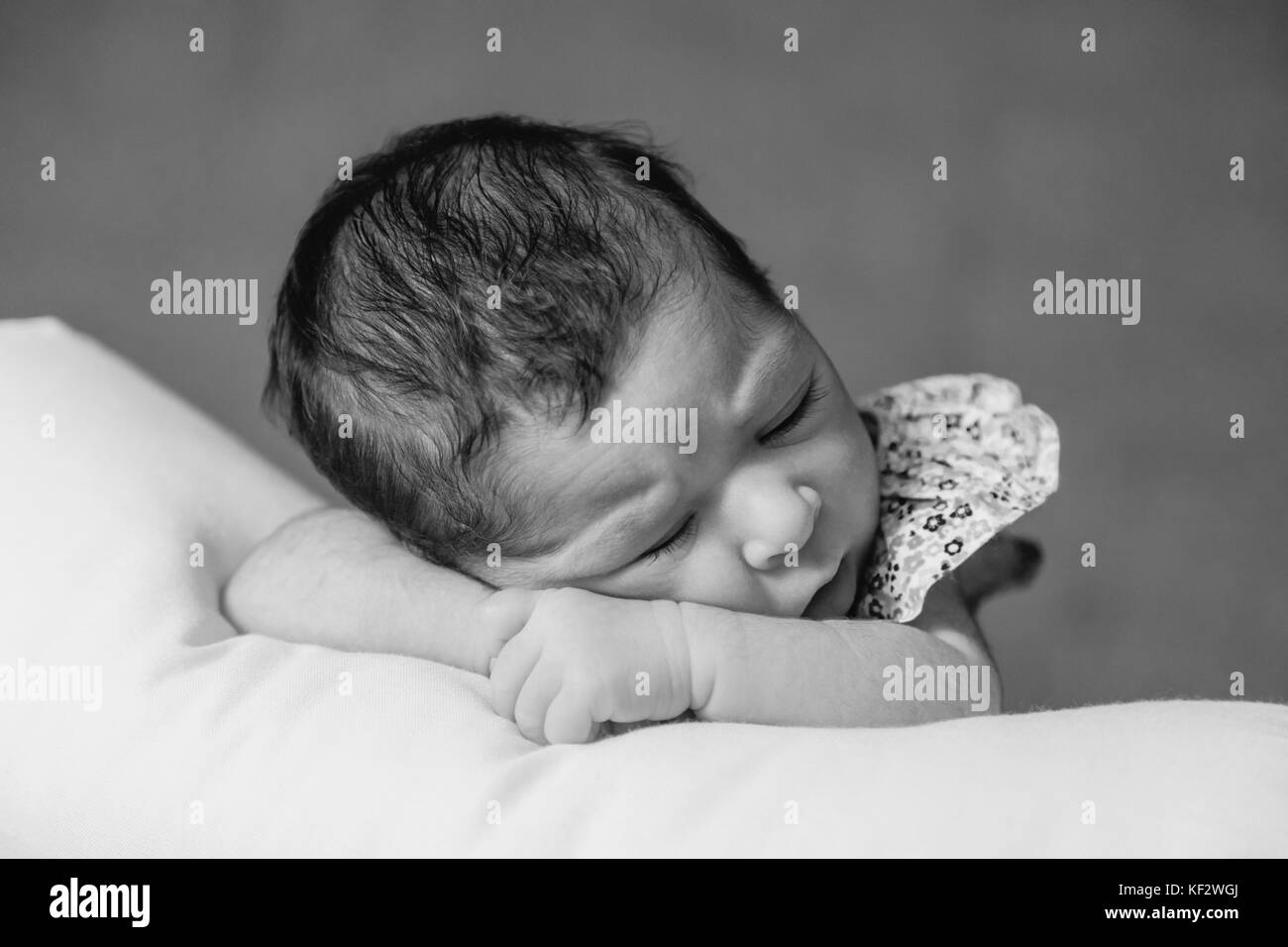 Close up portrait of a cute two weeks old newborn baby girl wearing a floral dress, sleeping peacefully over a pillow / newborn baby portrait cute Stock Photo