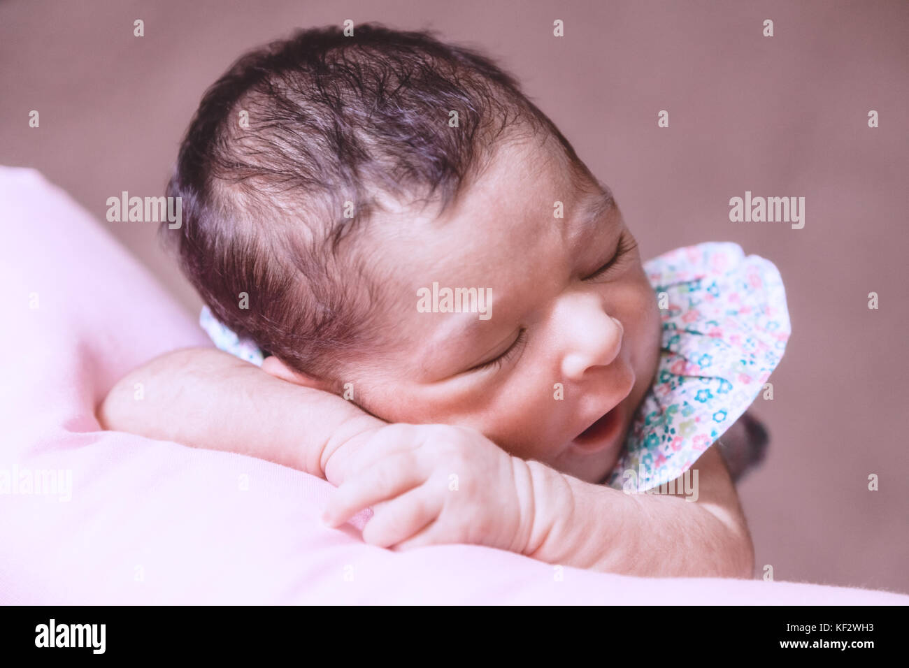 Close up portrait of a cute two weeks old newborn baby girl wearing a floral dress, sleeping peacefully over a pillow / newborn baby portrait cute Stock Photo