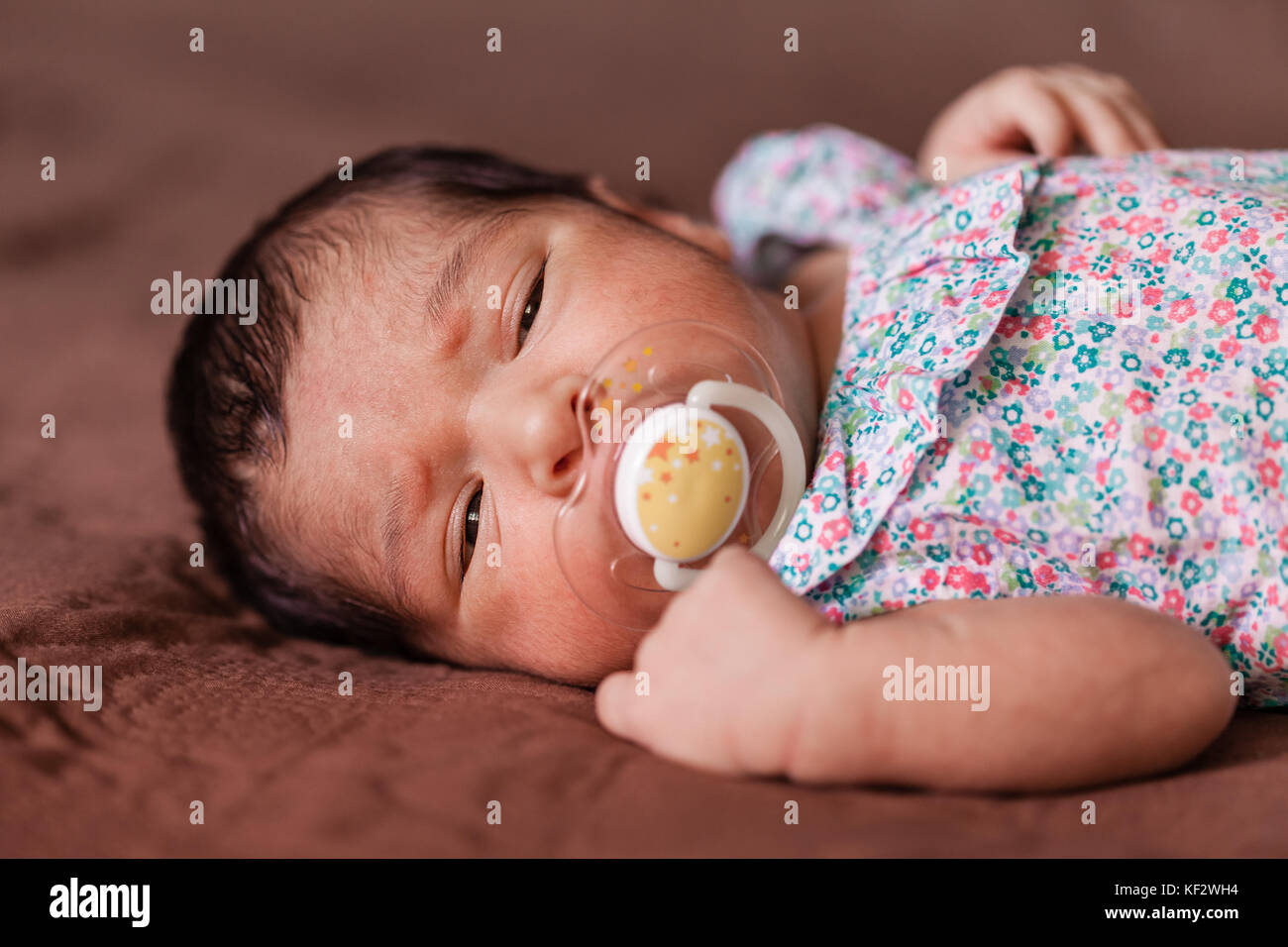 Close up portrait of a cute two weeks old newborn baby girl wearing a floral dress with sleepy eyes / newborn baby portrait cute girl sleepy drowsy Stock Photo