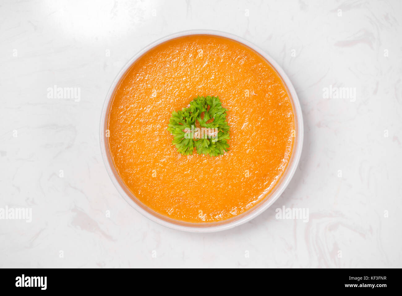 Carrot soup with cream and parsley on white stone background. Top view ...