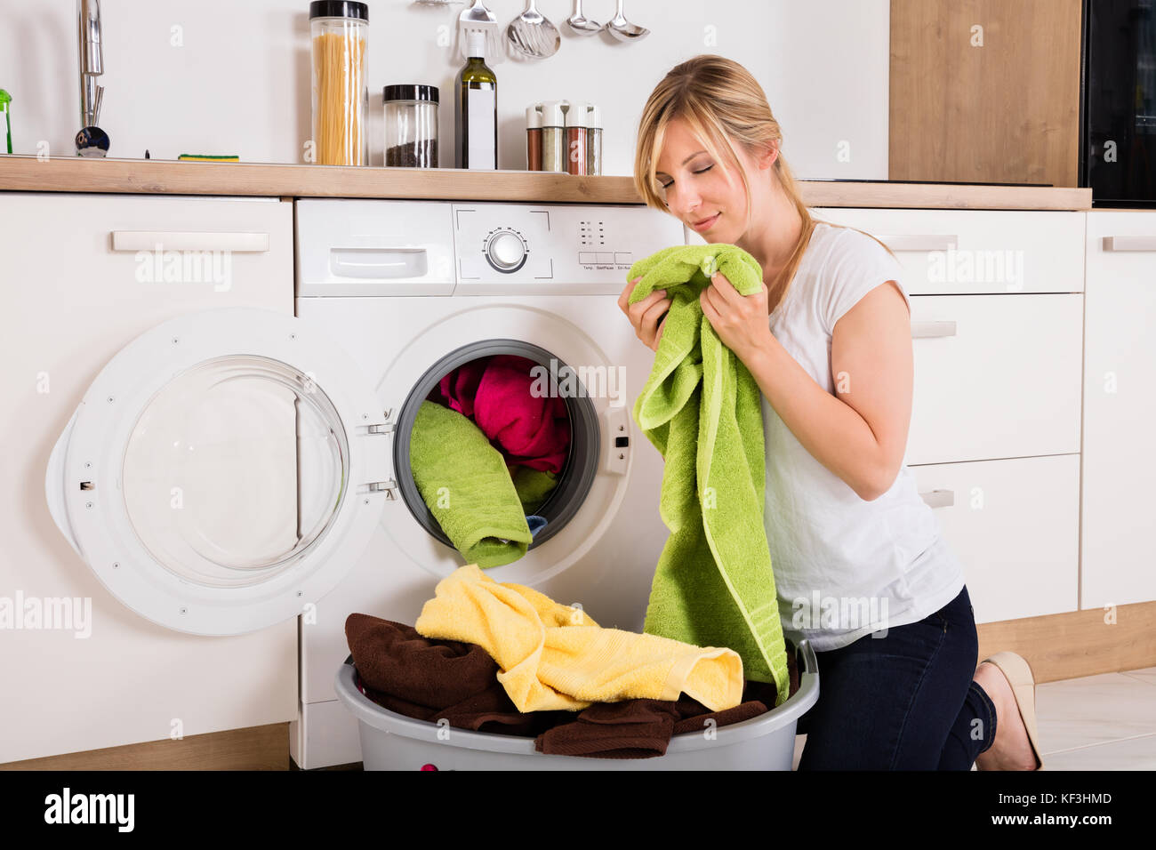 Young Woman Smelling Cleaned Clothes After Washing Near Washing Machine Stock Photo