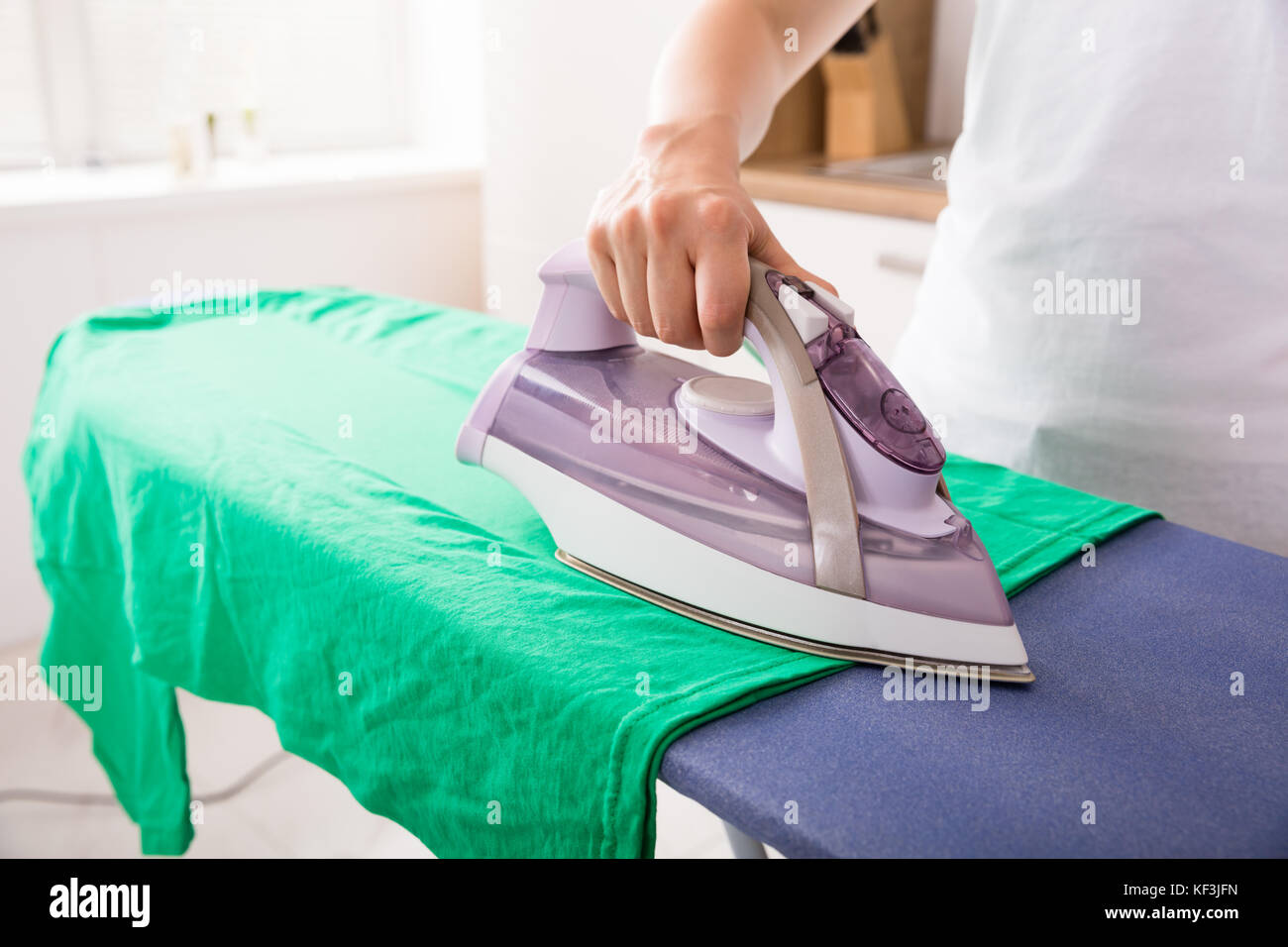 Close-up Of Young Woman Hand Ironing Green T-shirt At Home Stock Photo