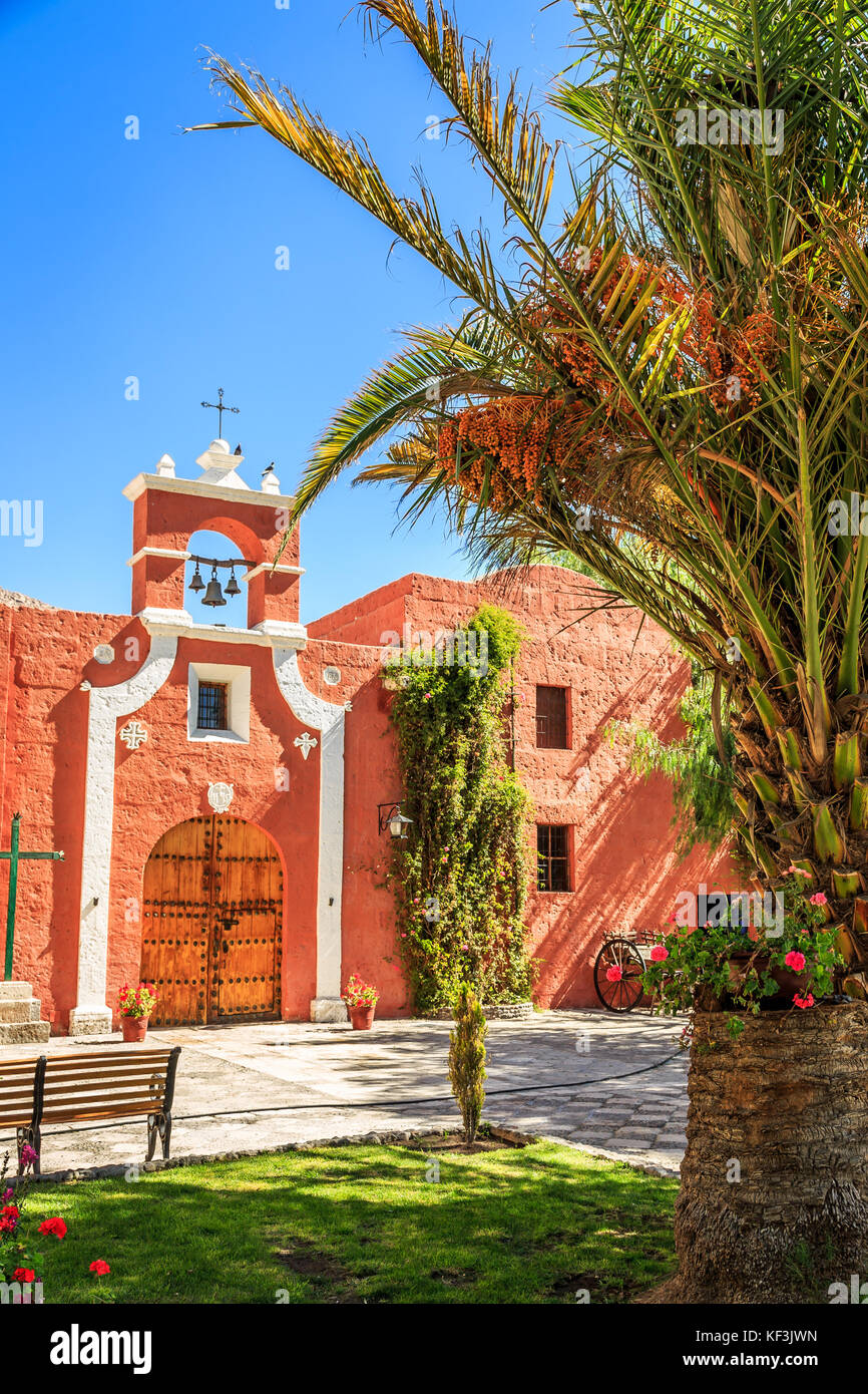 Red walls of Spanish catholic chapel with palms, trees and flowers, Arequipa, Peru Stock Photo