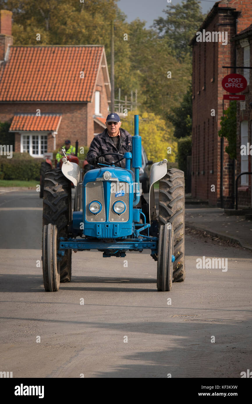 Man driving blue vintage tractor in parade through Bugthorpe village for annual charity event - Wolds Vintage Group Road Run, Yorkshire, England, UK. Stock Photo