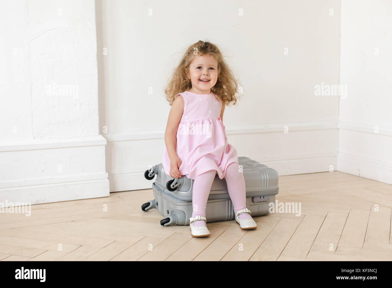 Adorable girl on suitcase in room Stock Photo