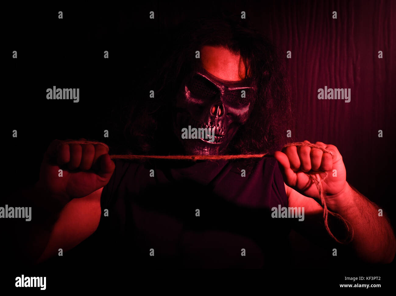 Halloween concept studio shoot with model having long hair holding a thread string with red light showering on it Stock Photo