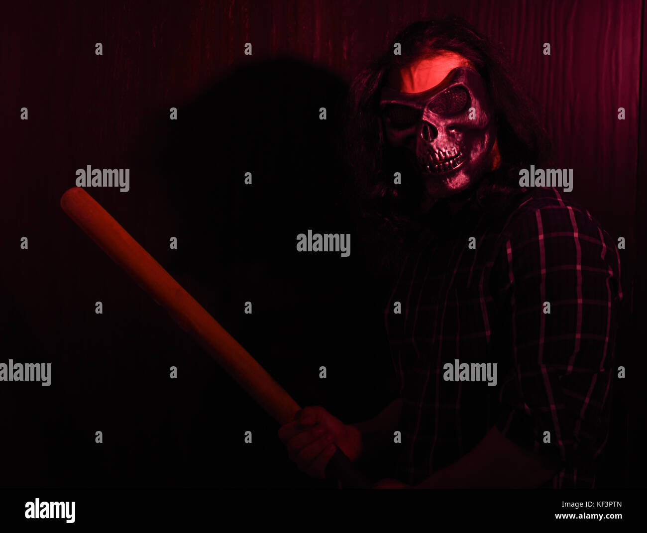 Halloween concept studio shoot with model having long hair holding a baseball bat with red light showering on it Stock Photo