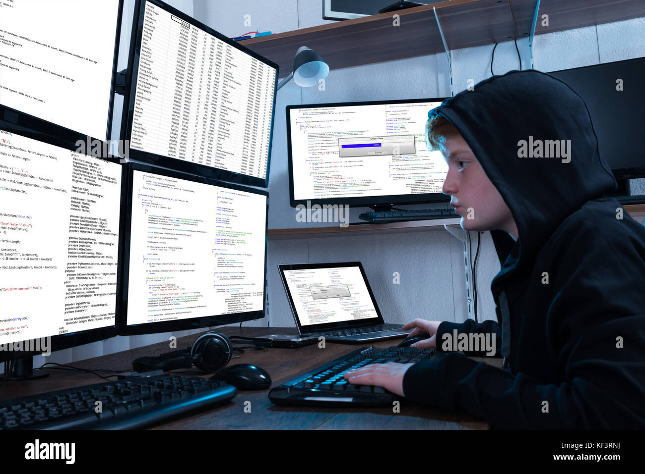 Boy Programming On Computer With Multiple Monitors And Laptop On Desk Stock Photo