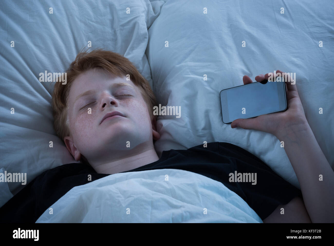 Boy Sleeping On Bed With His Mobile Phone Stock Photo