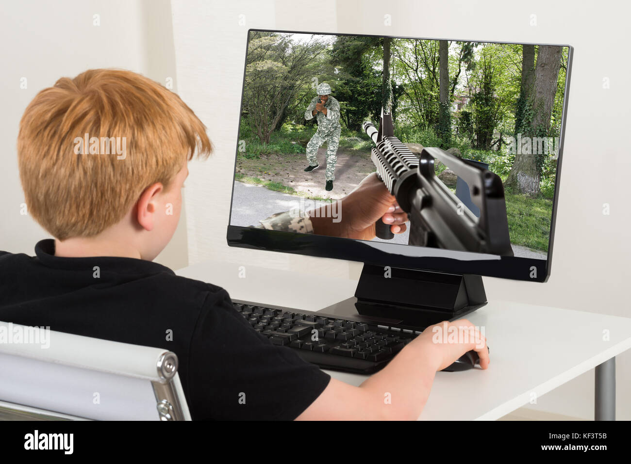 Boy Sitting On Chair Playing Action Game On Computer Stock Photo