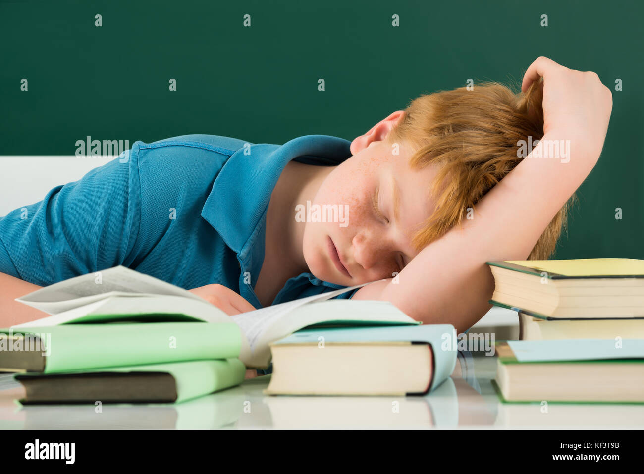Boy Sleeping In Classroom With Books On Desk Stock Photo