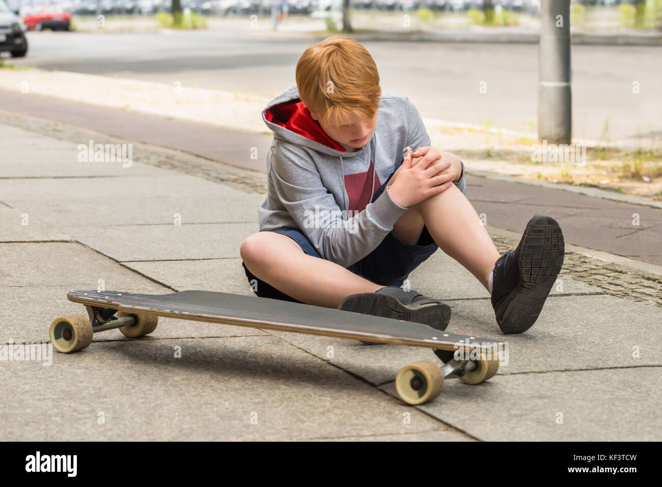 Boy Looking At His Injured Leg Sitting Near Skateboard Stock Photo