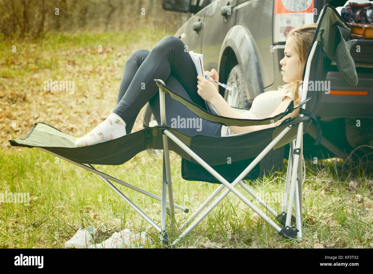 Young woman reading a book sitting in a chair outdoors Stock Photo - Alamy