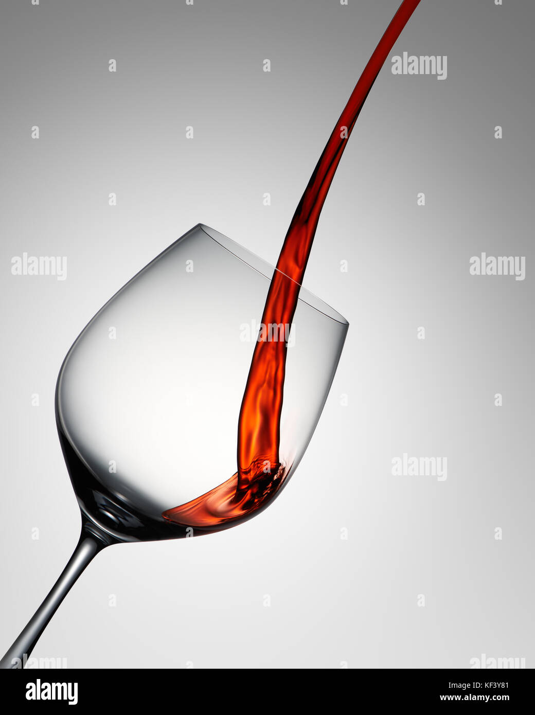 Red wine poured into elegant wine glass on grey gradient Stock Photo