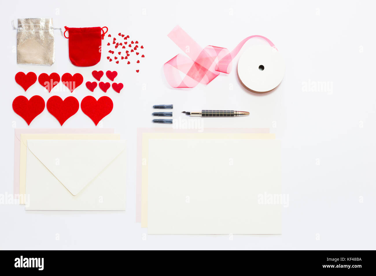 Display of love letter items on white background. Assortment of cards, envelopes, hearts, ribbon and ink pen. Stock Photo