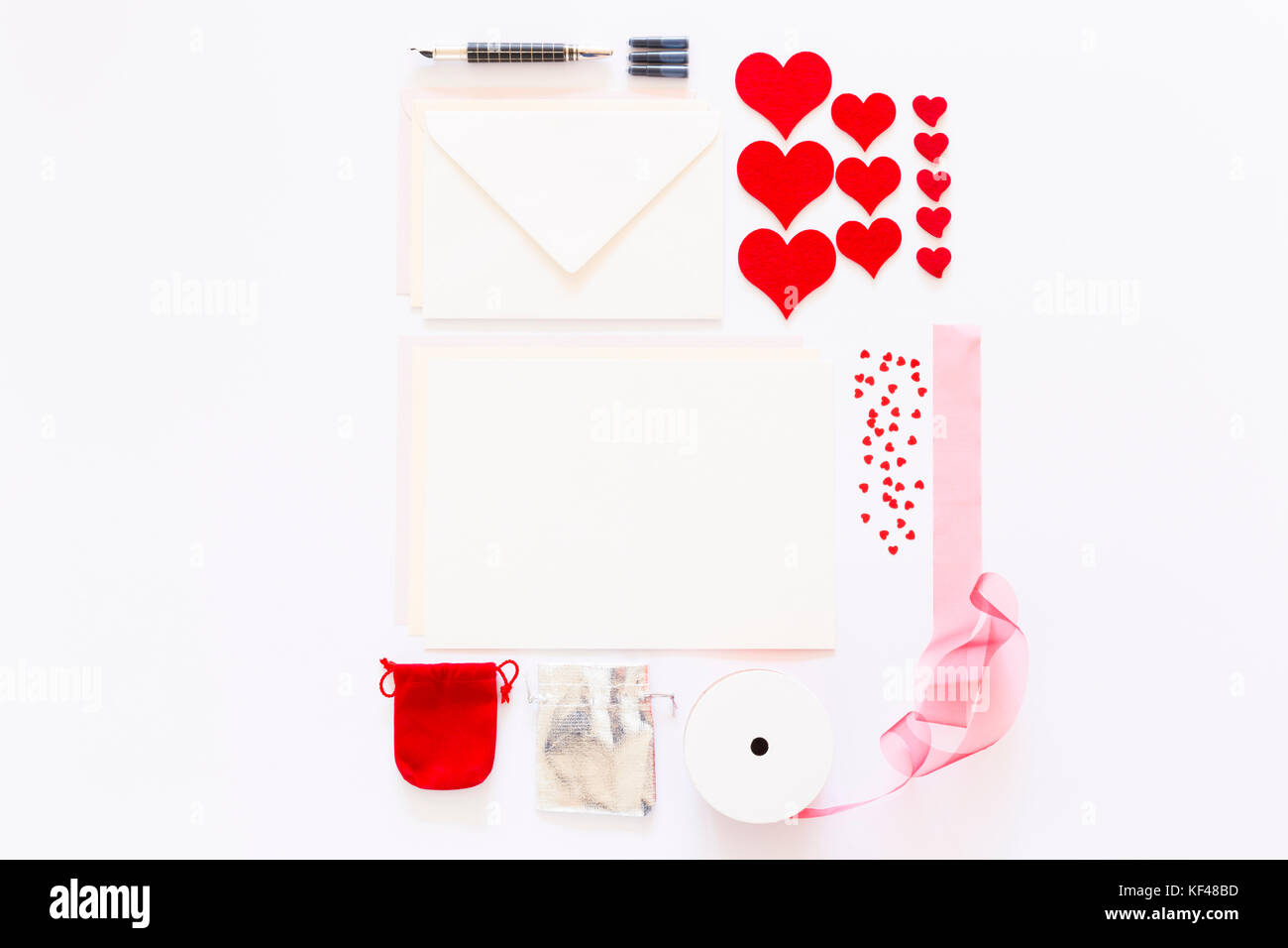 Display of love letter items on white background. Assortment of cards, envelopes, hearts, ribbon and ink pen. Stock Photo