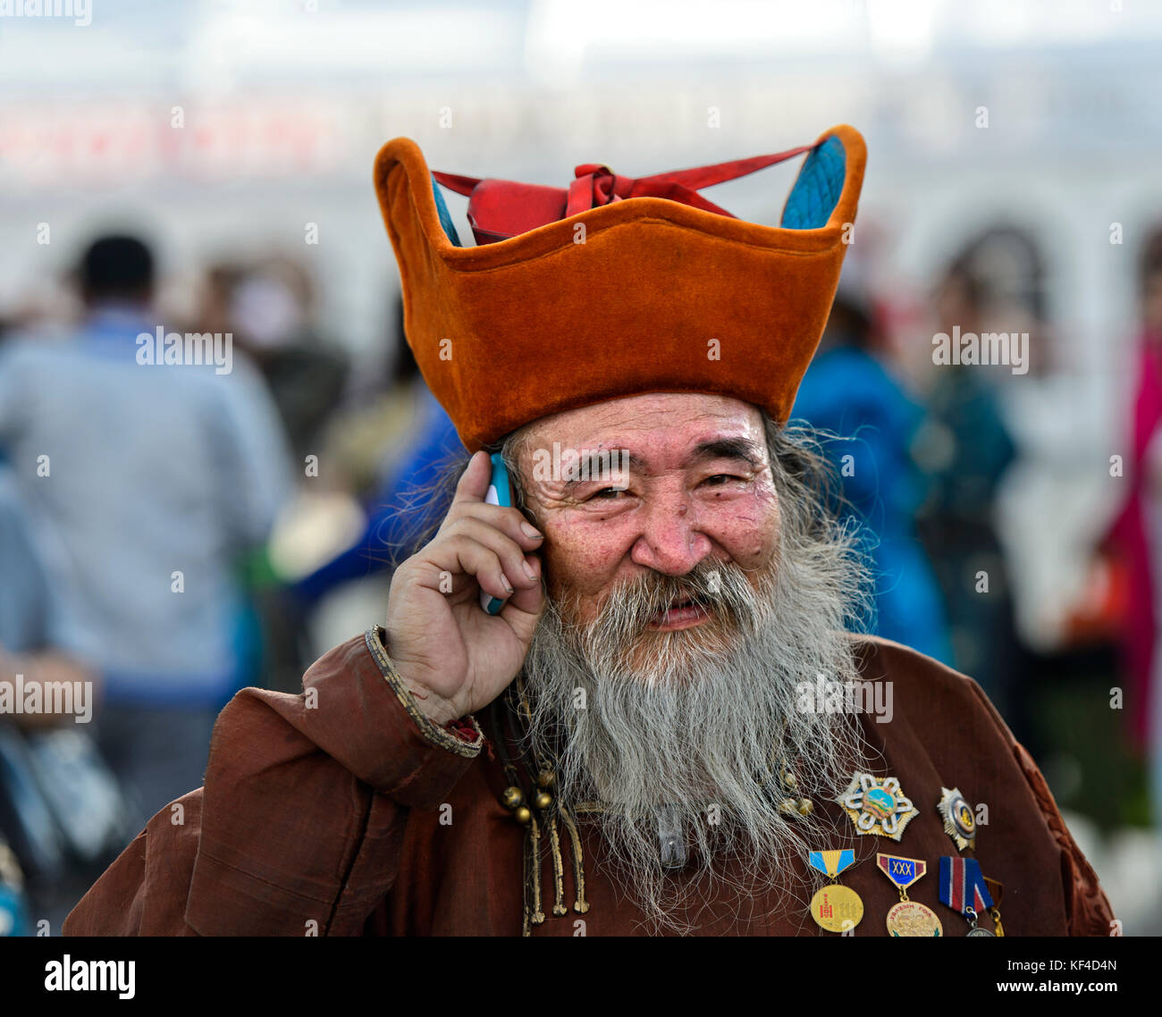 Elderly man with beard, head-dress and medals is talking on a mobile phone, Ulaanbaatar, Mongolia Stock Photo