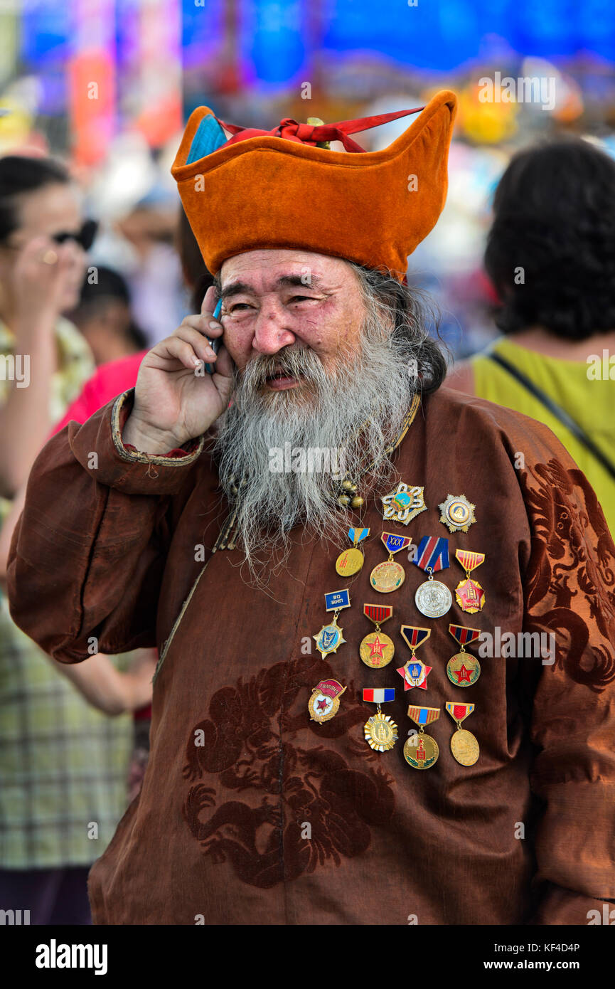 Elderly man with beard, head-dress and medals is talking on a mobile phone, Ulaanbaatar, Mongolia Stock Photo