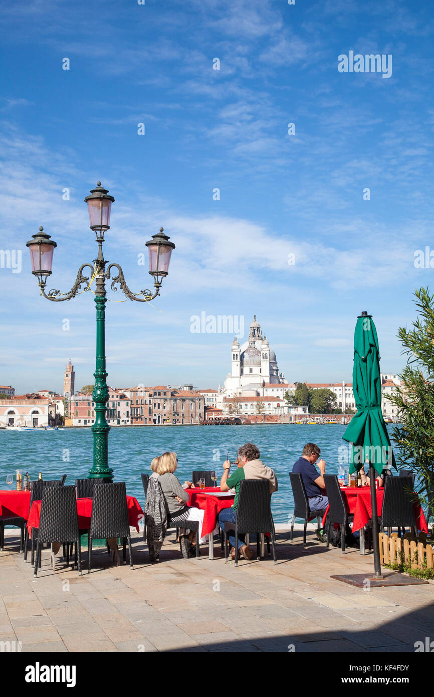People enjoying drinks at an open air restaurant on Giudecca Island, Venice, Italy overlooking the Giudecca Canal, Zattere and Basilica Santa Maria de Stock Photo