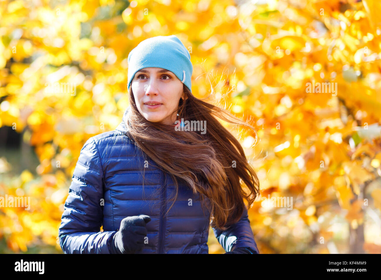 Young happy woman running in autumn park against yellow foliage tree ...