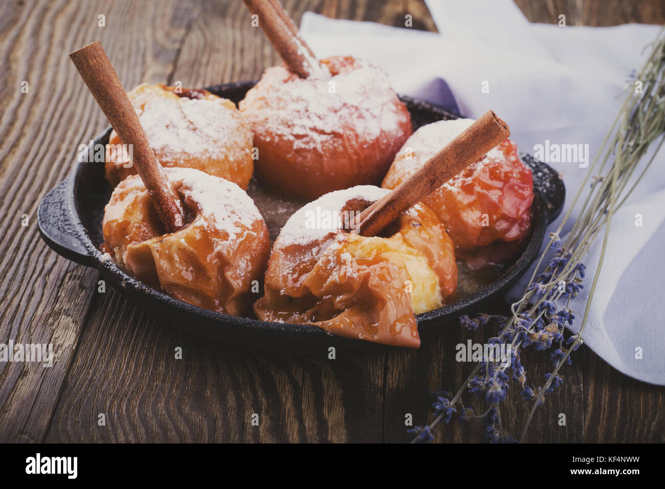 Caramelized baked apples with cinnamon sticks in cast iron skillet on rustic wooden background Stock Photo