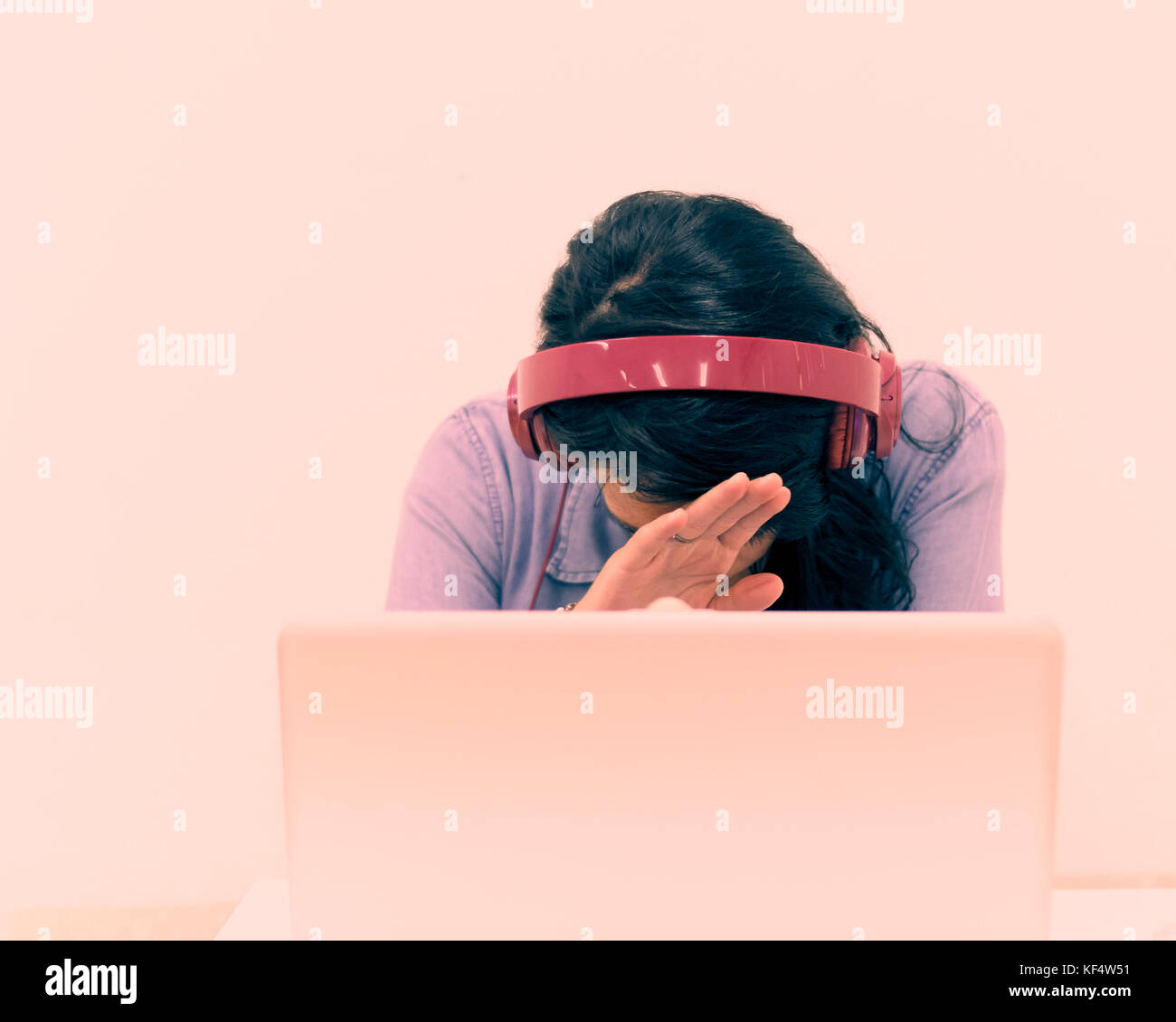 Young woman working at a laptop while wearing headphones and covering ...