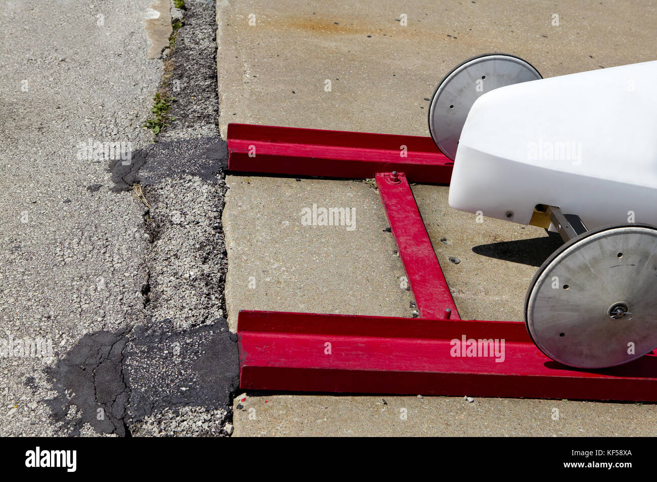 Front wheels of a white aerodynamic Soap Box Derby racer on a red metal track on a ramp ready for a time trial competition race Stock Photo