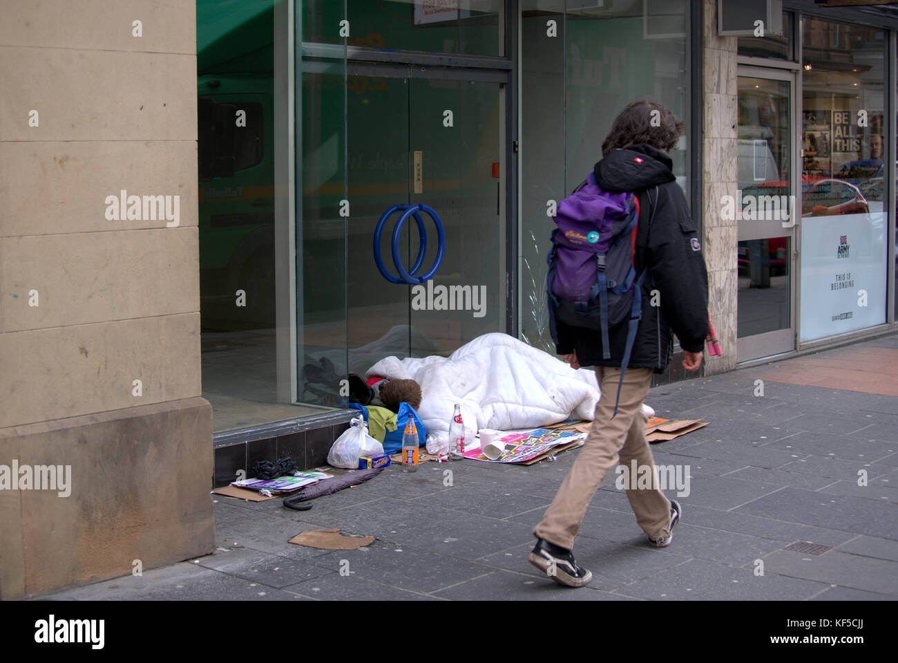 Glasgow young homeless boy looks dead as he sleeps on ground in doorway unconscious as strangers walk by on street in duvet Stock Photo
