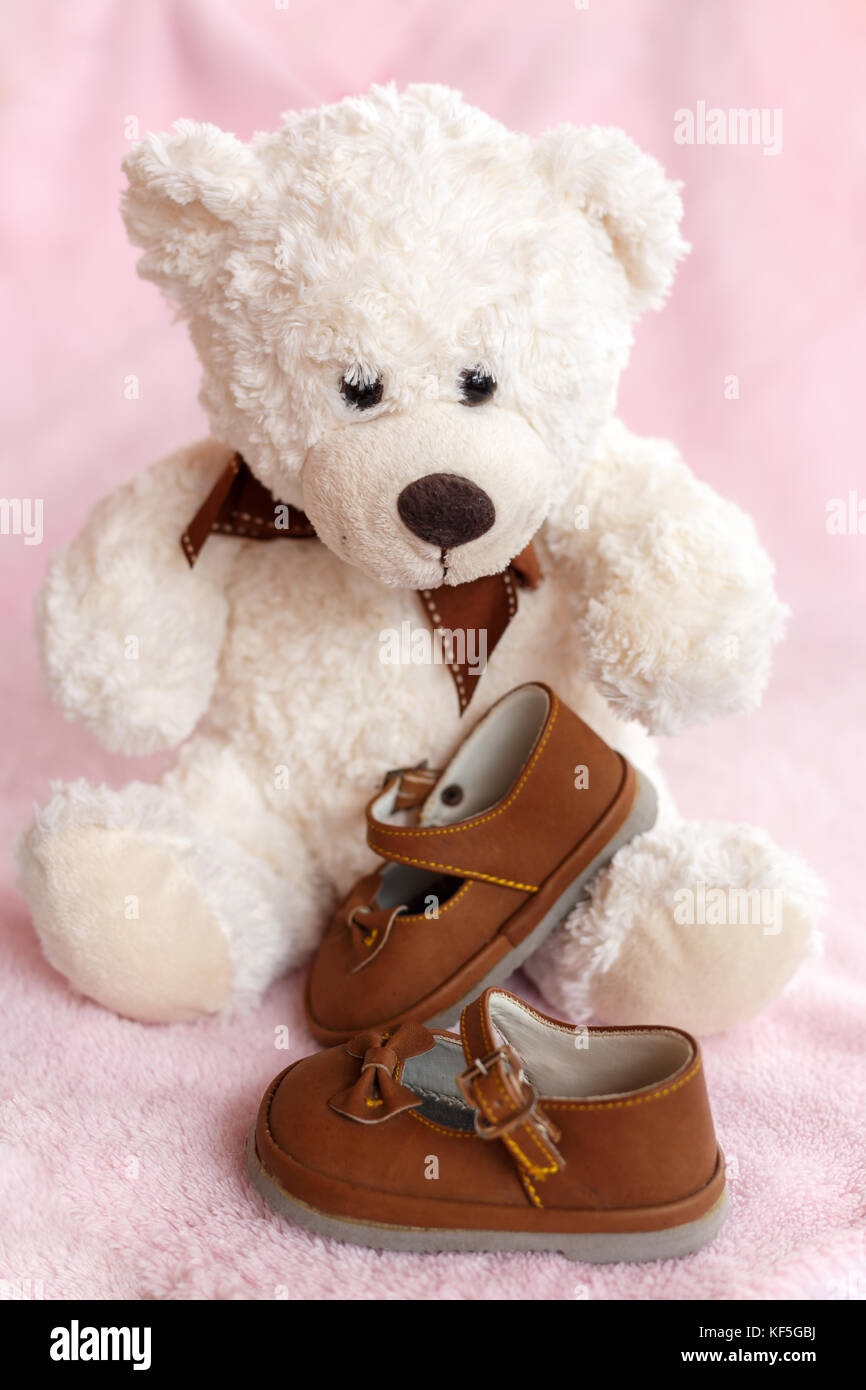 Teddy bear with pair of Mary Jane style baby shoes against a pale pink background. Stock Photo