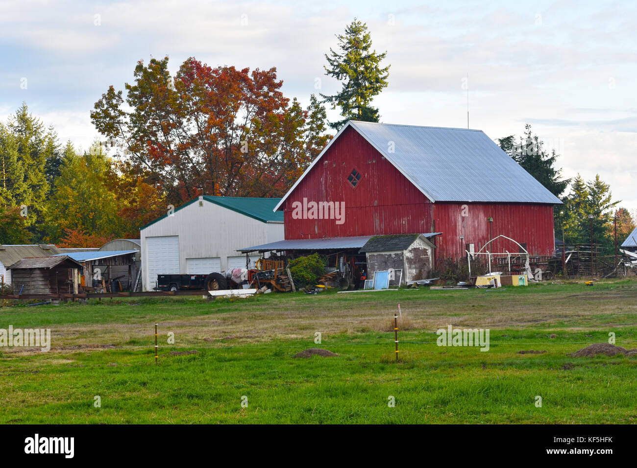 A red barn with lots of junk in front, farm equipment, an electric fence.  Mole holes are in the foreground in this autumn scene. Stock Photo