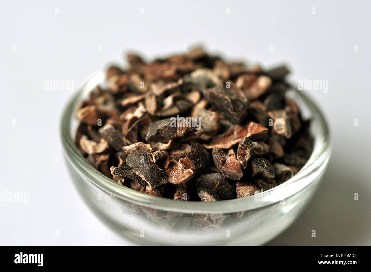 Raw cacao bean (Theobroma cacao) nibs in a glass bowl, isolated on
