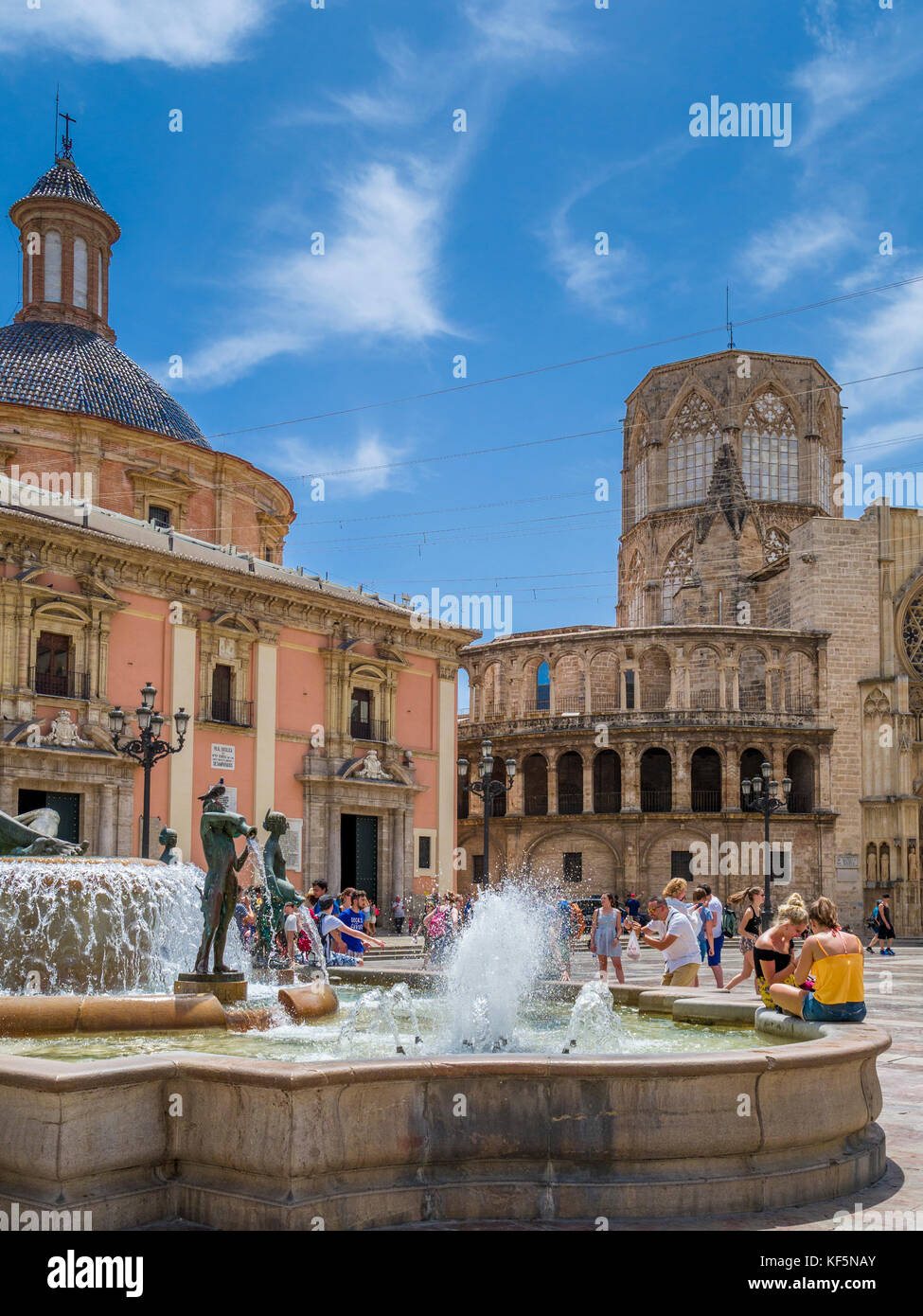 Tourists sitting by Turia fountain in la Plaza de la Virgen situated by the Cathedral (right) and Basilica Virgen de los Desamparados (left), Valencia Stock Photo