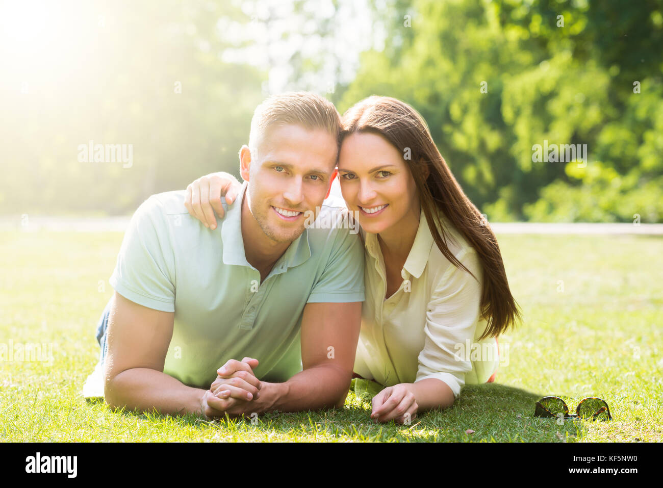 Happy Young Couple Lying On Green Grass At Park Stock Photo