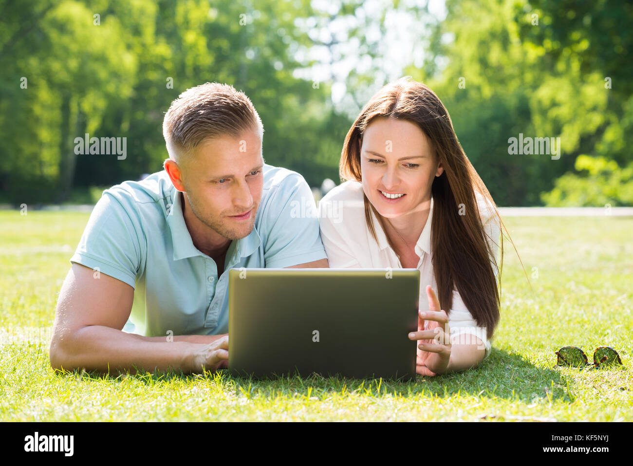Young Couple Lying On Grass Using Laptop At Park Stock Photo - Alamy