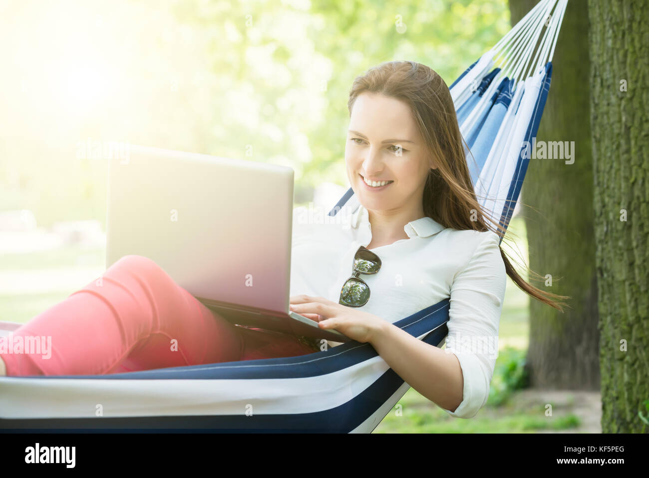 Smiling Woman Using Laptop While Lying In Hammock Stock Photo - Alamy