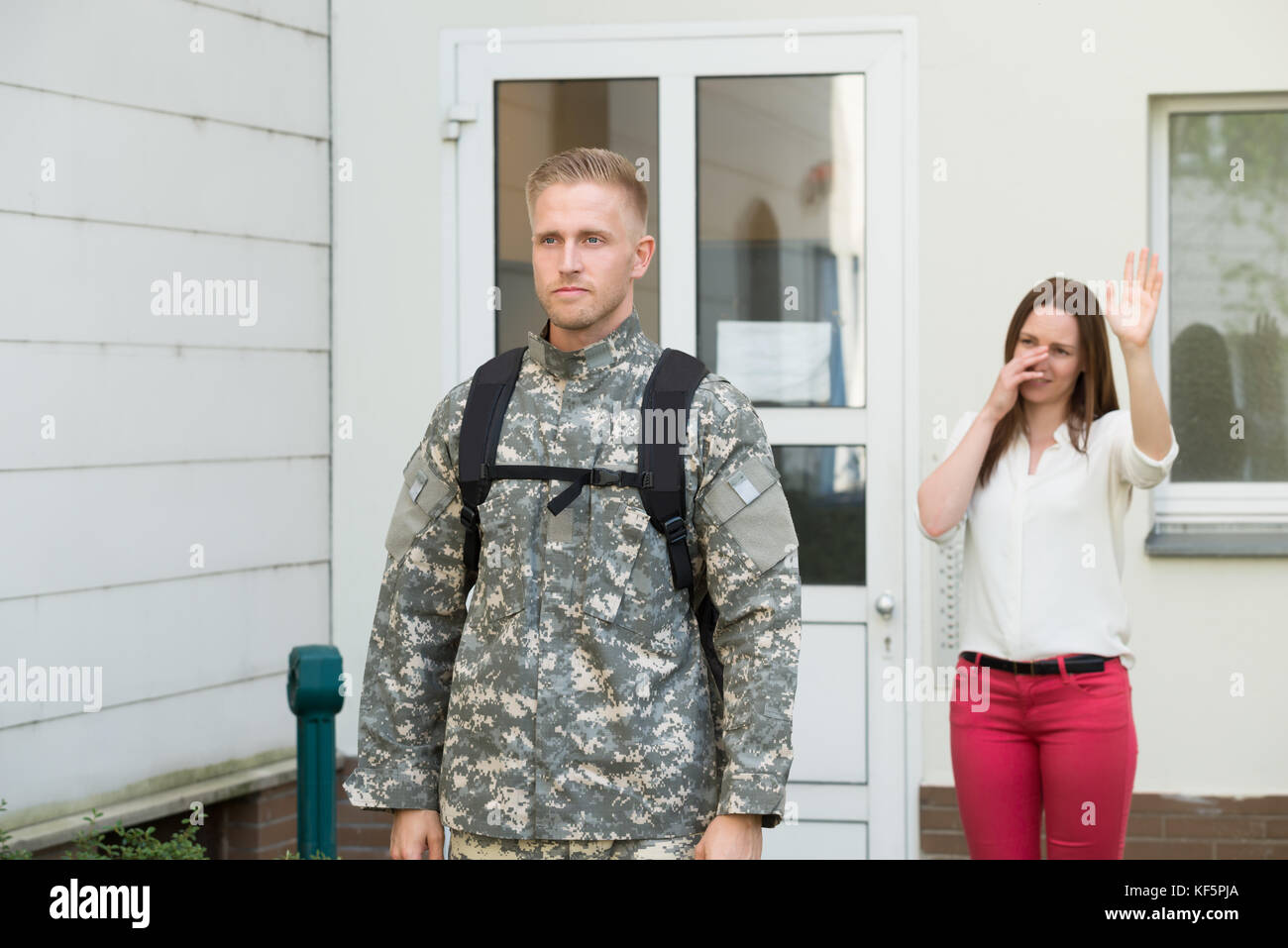 Unhappy Young Wife Waving Goodbye To Male Soldier Outside House Stock Photo