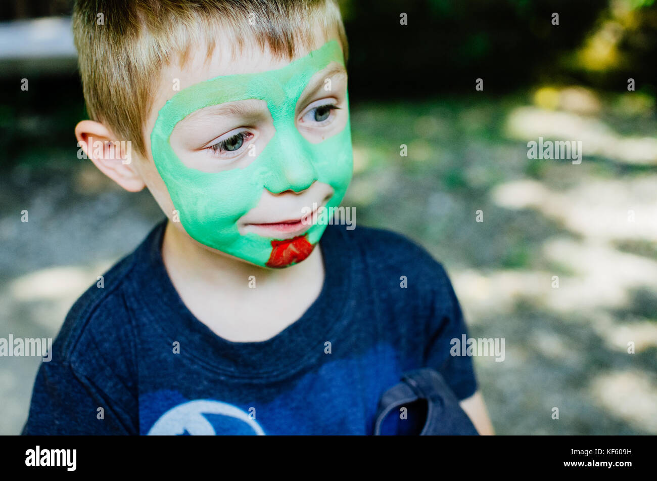 A boy with green face paint being painted Stock Photo